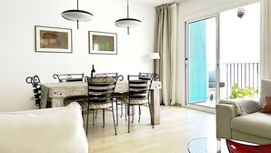 A dining area with a table and chairs, a sofa, a glass coffee table, and a balcony with a view. - Abbott apartment - 100m2 - 3 bedrooms, living room, 2 terraces, 1 min to beach (Sitges)