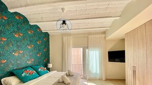A bedroom with a bed, a ceiling fan, a TV mounted on the wall, and a view of the outside. - Abbott apartment - 100m2 - 3 bedrooms, living room, 2 terraces, 1 min to beach (Sitges)