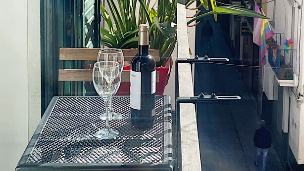 A balcony with a table, a bottle of wine, and a potted plant with flowers. - Abbott apartment - 100m2 - 3 bedrooms, living room, 2 terraces, 1 min to beach (Sitges)