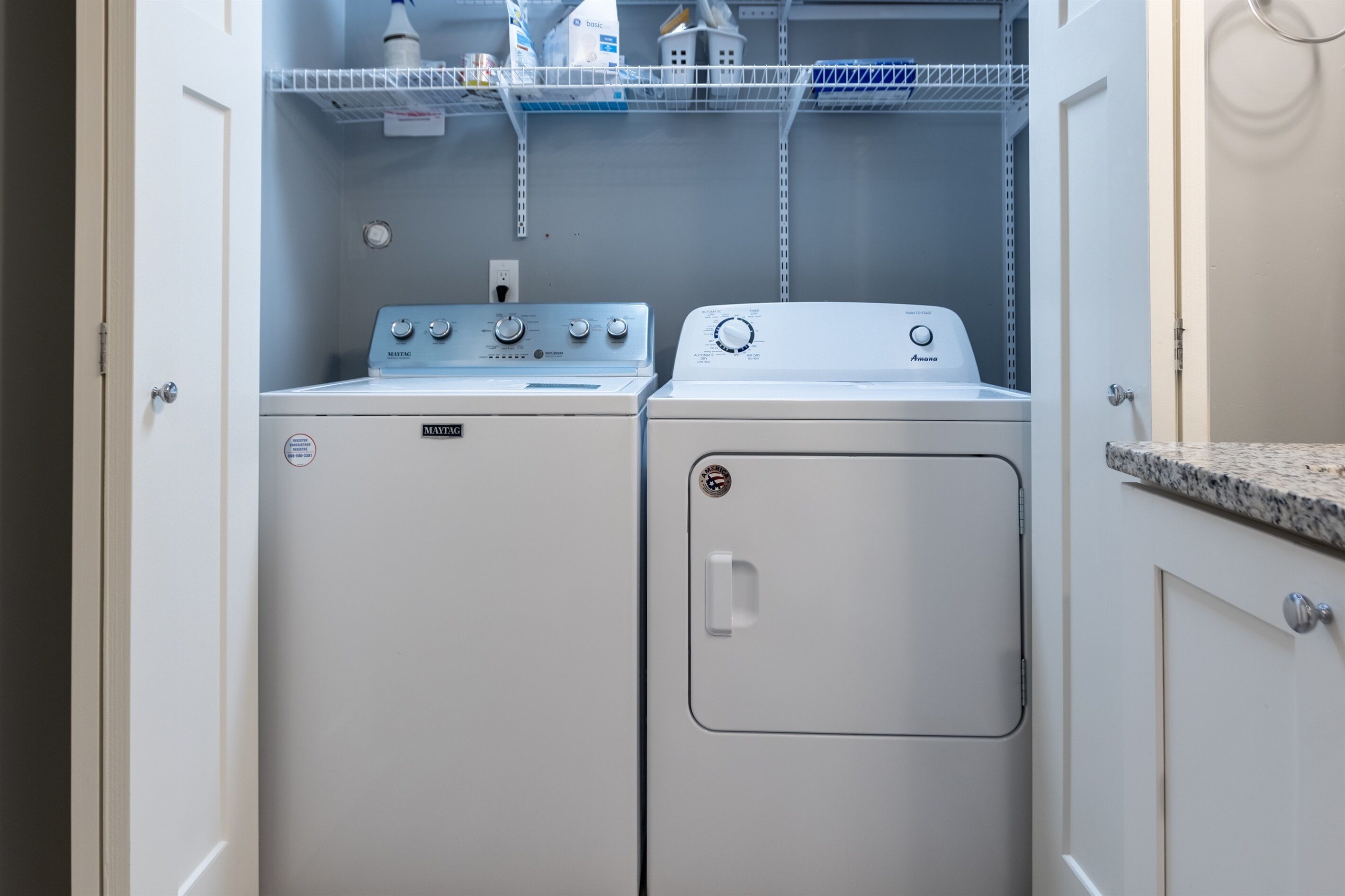 A laundry room with two washing machines, one labeled Maytag and the other Amana.
