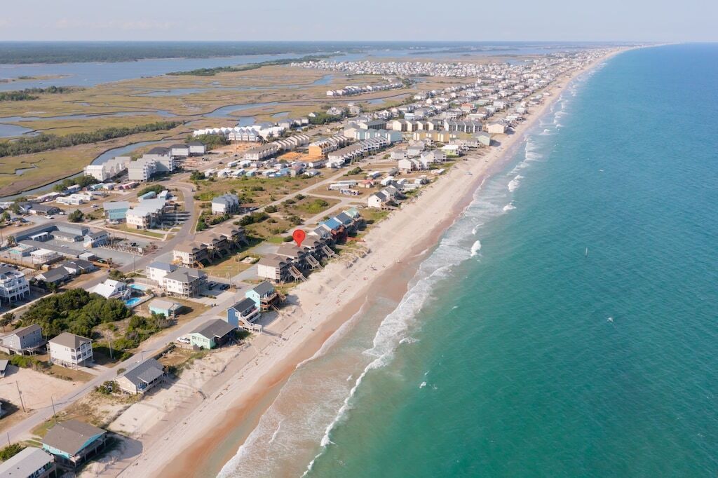 An aerial view of a coastal town with a beachfront, residential buildings, and industrial structures.