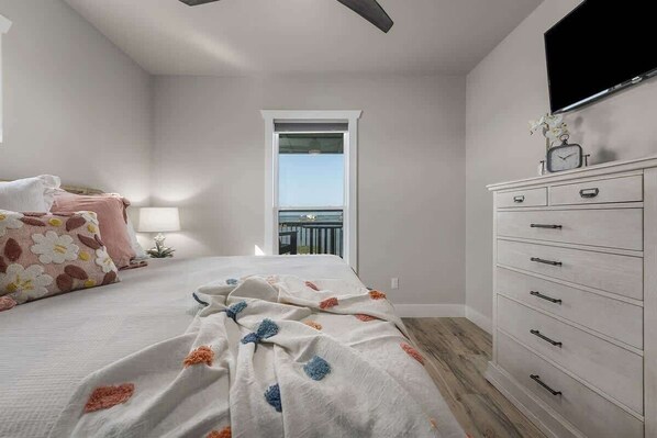 A bedroom with a bed, a dresser, a window, and a balcony.
