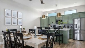 A modern kitchen with green cabinets, a stainless steel refrigerator, and a dining area with a white table and black chairs. - Luxury Lake Retreat w/ Pool, Spa, Kayaks & Views! (Rockport)