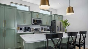 A modern kitchen with green cabinets, stainless steel appliances, and a central island with bar stools. - Luxury Lake Retreat w/ Pool, Spa, Kayaks & Views! (Rockport)