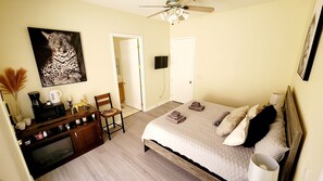 Une chambre à coucher comprenant un lit, un bureau avec une chaise, un téléviseur et un ventilateur de plafond.