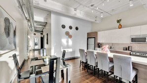 Una cocina moderna con electrodomésticos de acero inoxidable, un comedor con mesa de vidrio y un pasillo con vista a otra habitación.
