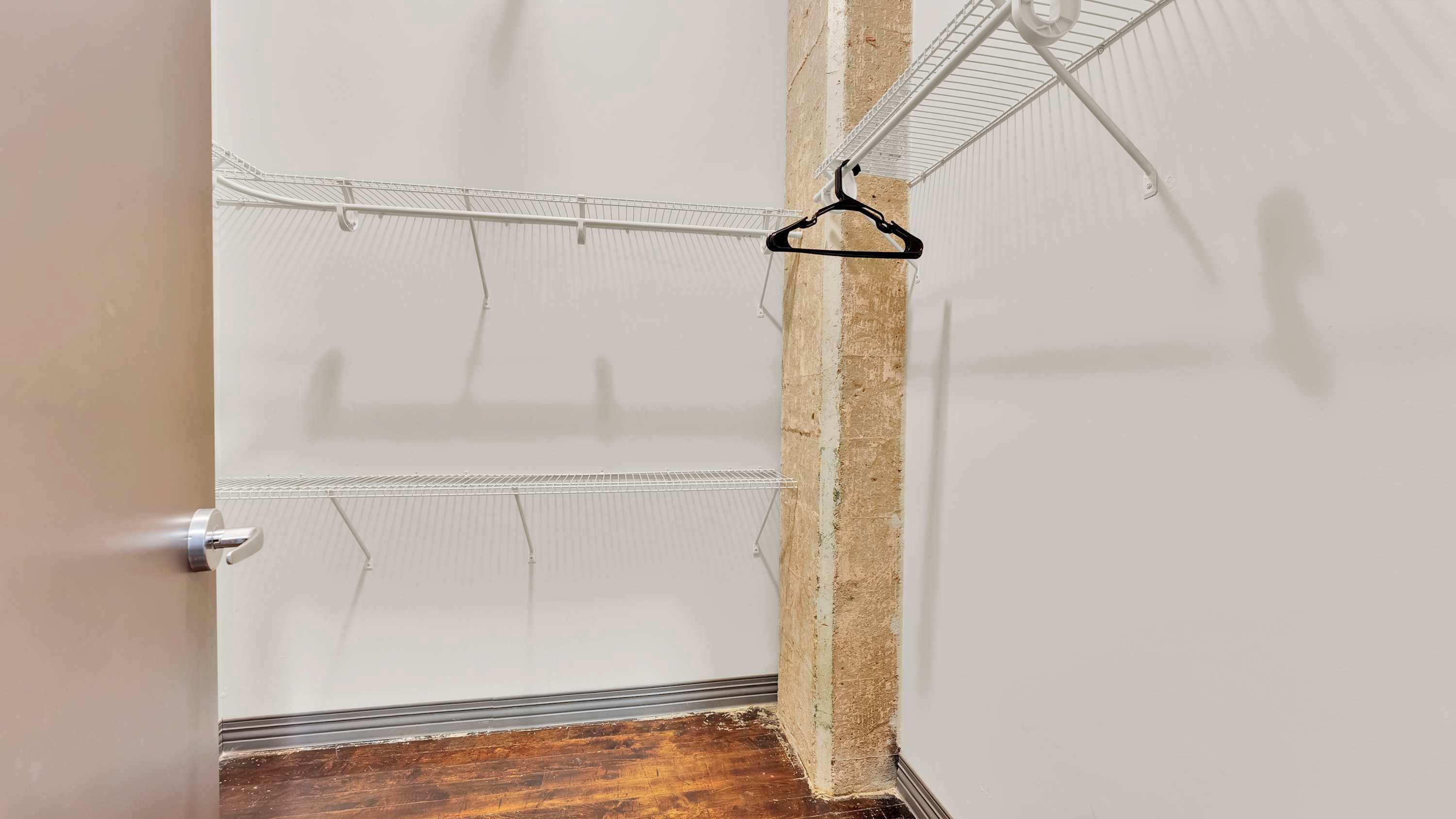 A room with a metal wire shelf and a black hanger.