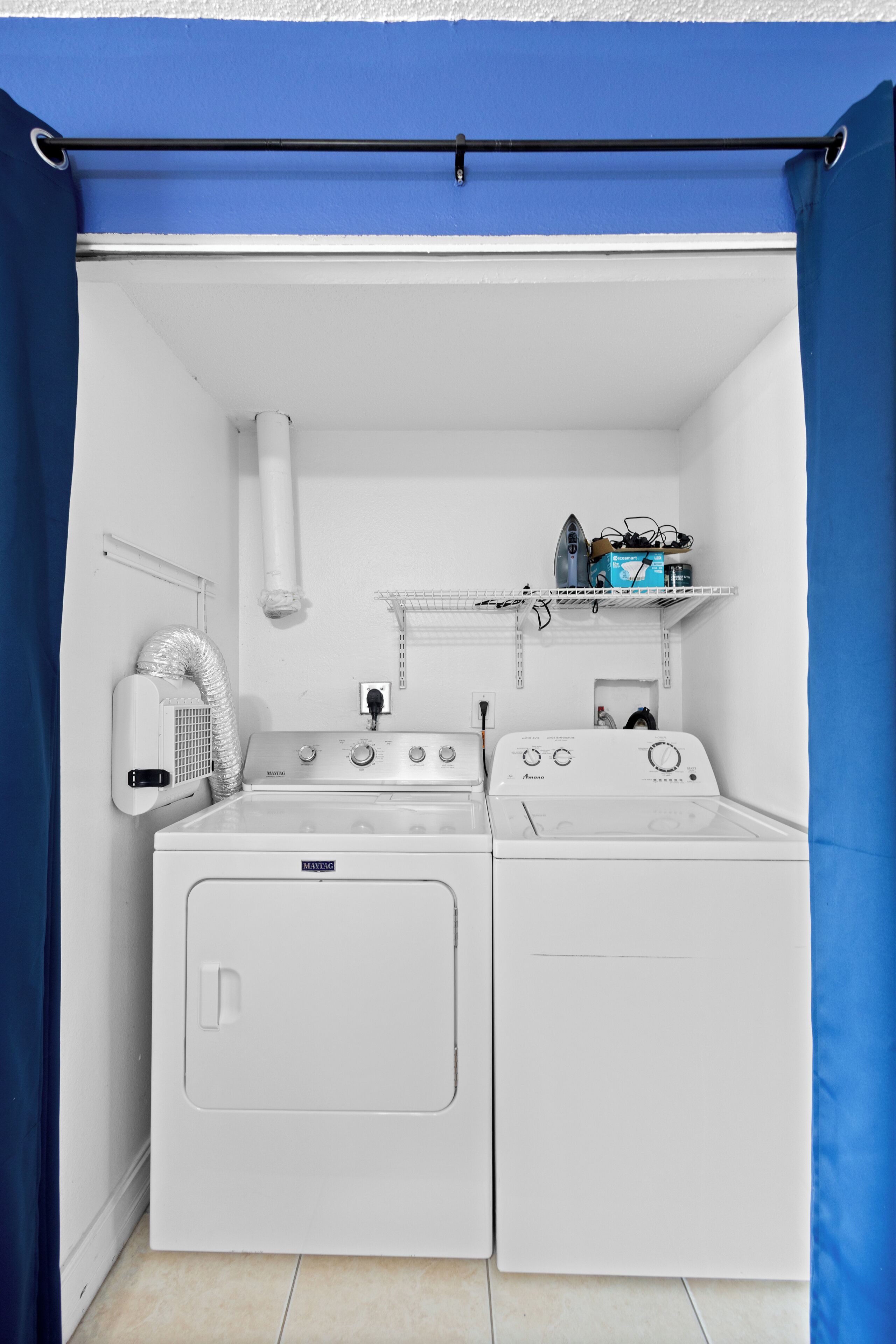 Une petite buanderie comprenant un lave-linge, un sèche-linge et une petite étagère où sont rangés les produits d’entretien.
