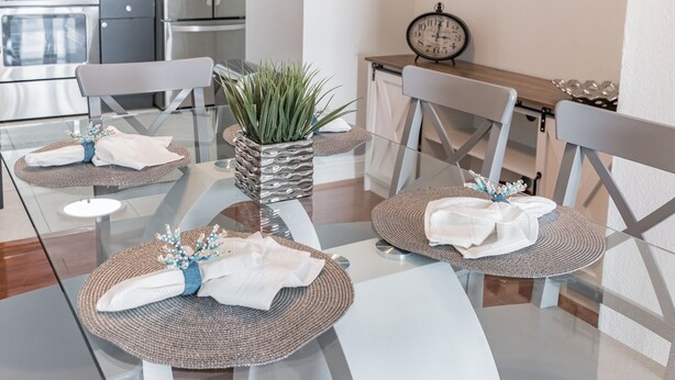 Un comedor moderno con una mesa de vidrio, individuales tejidos y servilletas blancas dobladas con esmero.