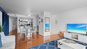 Una sala de estar moderna con un televisor de pantalla plana, un sofá blanco y una zona de comedor con sillas y una mesa.