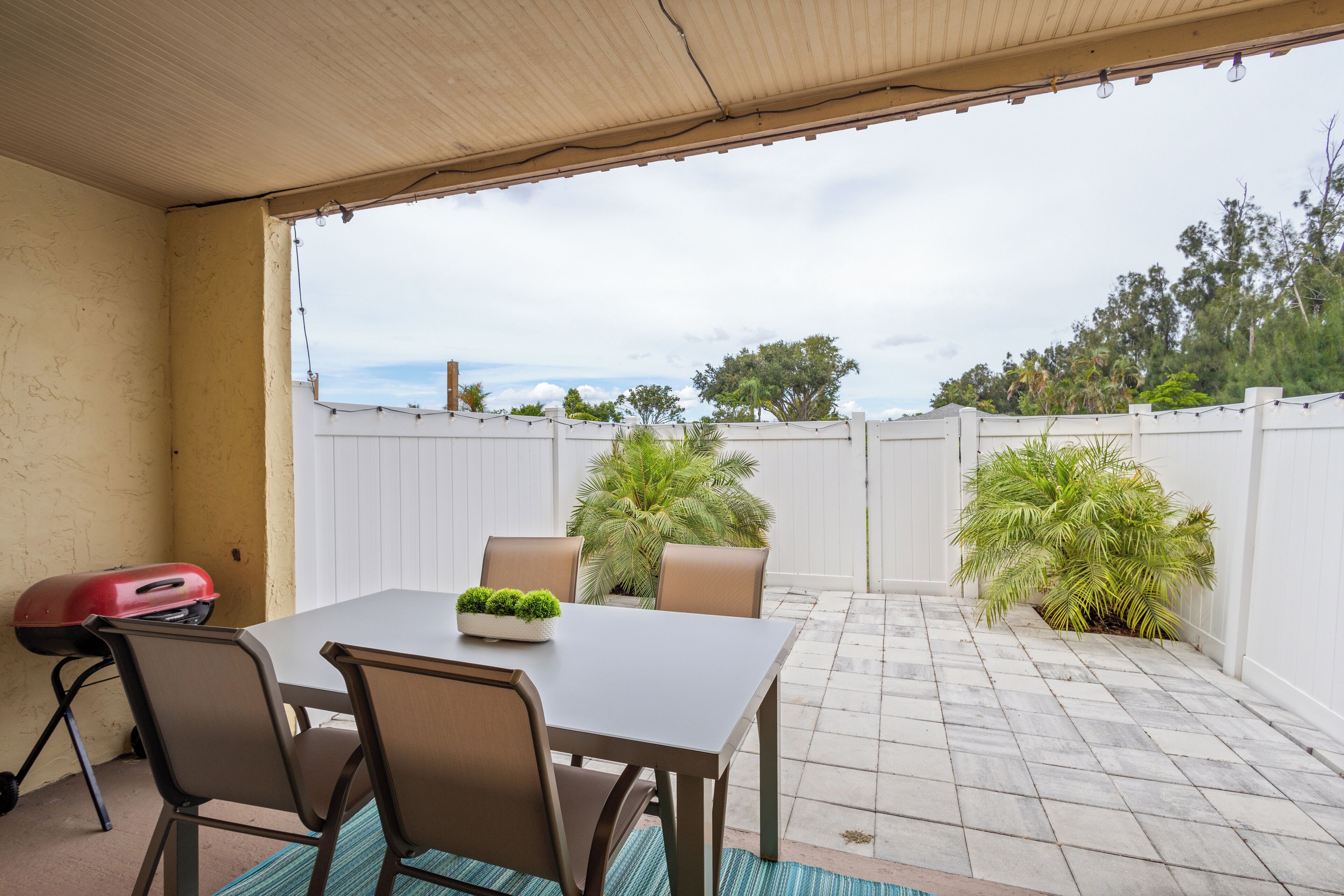 An outdoor patio with a table and chairs, a grill, and potted plants.