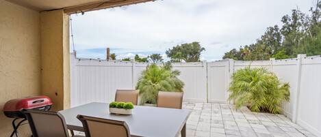 An outdoor patio with a table and chairs, a grill, and potted plants.