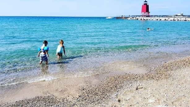 Une plage à l’eau claire, un phare rouge et une jetée.