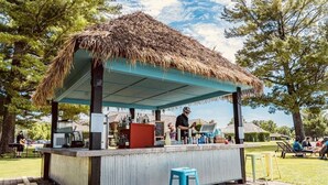 Un bar de style tiki avec un toit de chaume, un comptoir et des tabourets.