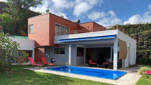 Et moderne hus med to etager, en overdækket terrasse og en swimmingpool.