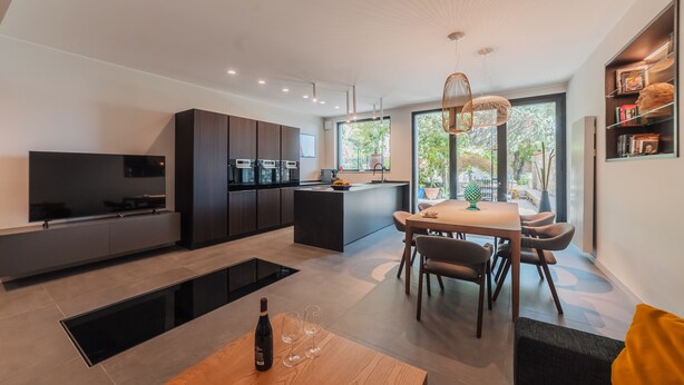A modern kitchen with dark cabinetry, a central island, and a dining area with a table and chairs. - In the heart of the town (Taormina)