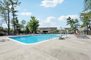 A rectangular swimming pool with a clear blue water surface, surrounded by a concrete deck with lounge chairs and umbrellas. - Luxury Duplex Apartment - Free Garage parking close to DC (Alexandria)