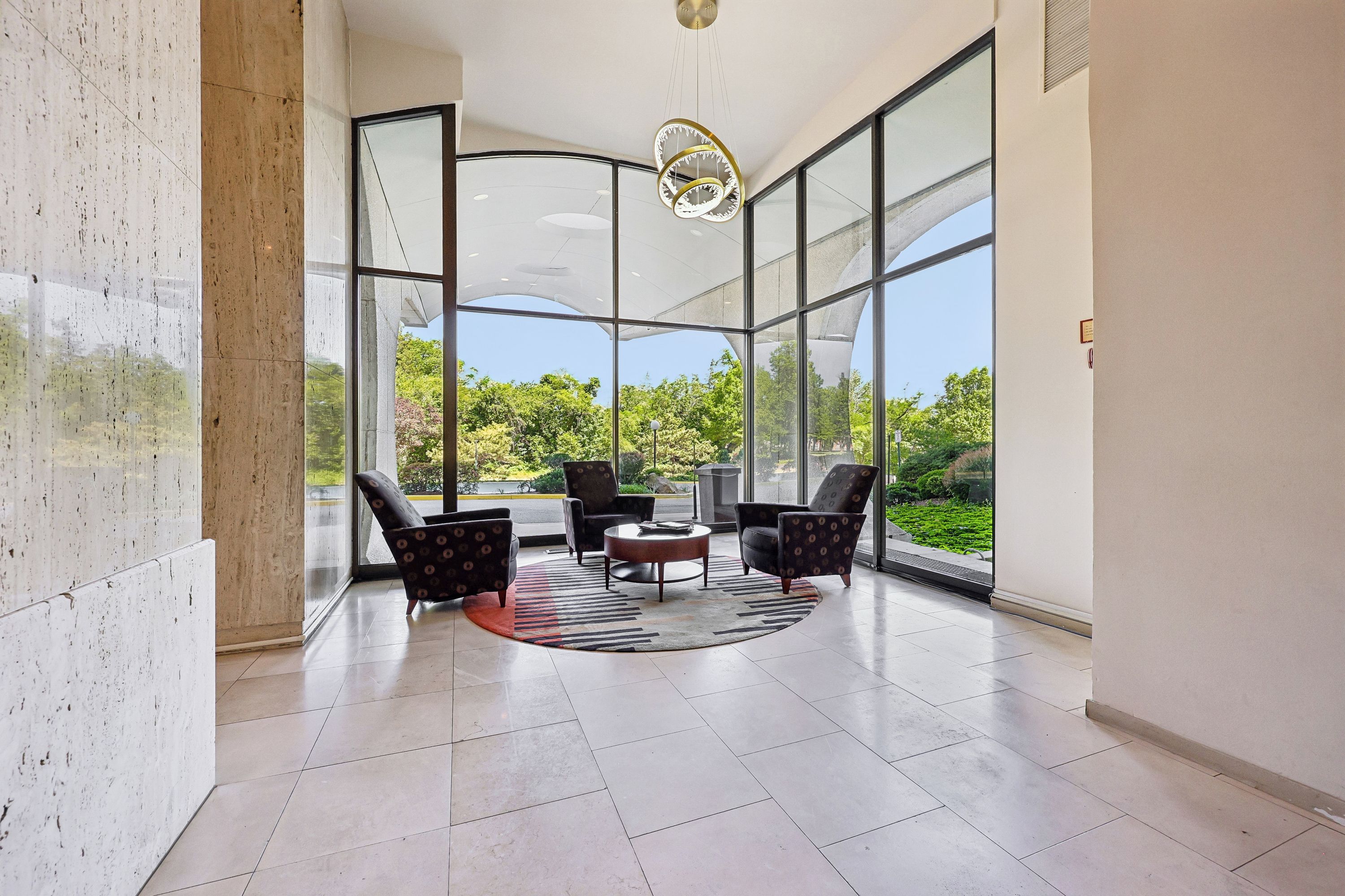 A modern interior with large windows, a round coffee table, and two patterned armchairs.