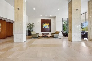 A spacious lobby with a modern design, featuring a central seating area with sofas and a coffee table, flanked by large pillars and a large window offering a view of the outdoors. - Luxury Duplex Apartment - Free Garage parking close to DC (Alexandria)