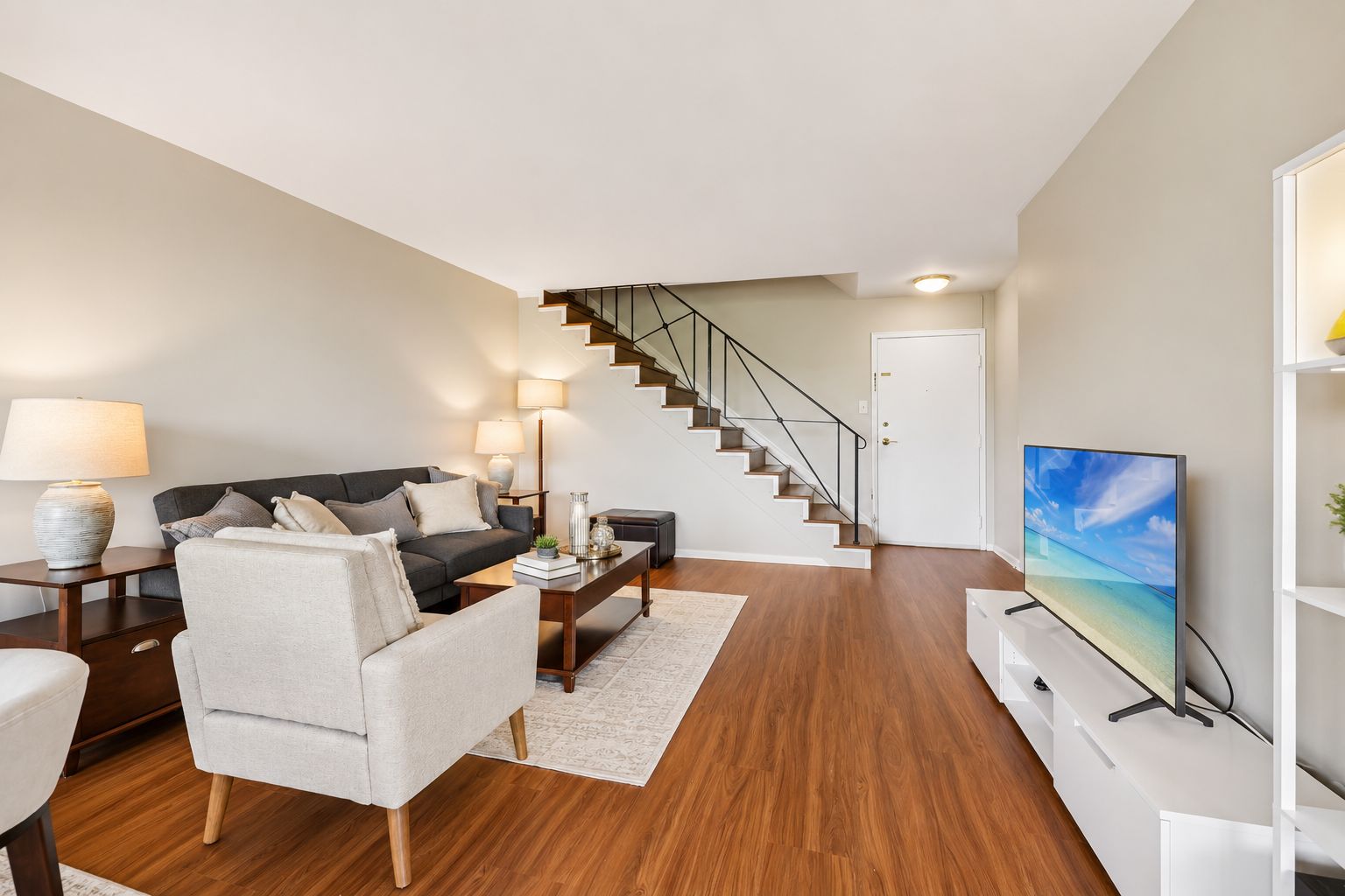A modern living room with a sofa, armchair, coffee table, and a flat-screen TV.