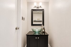 A bathroom with a glass bowl sink, a black cabinet, a mirror above the sink, and a door on the left. - Luxury Duplex Apartment - Free Garage parking close to DC (Alexandria)