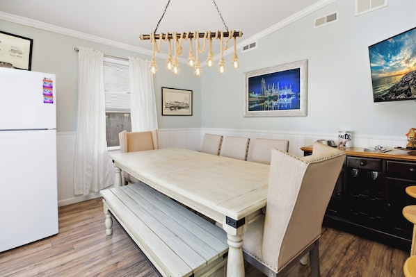 A dining area with a wooden table and benches, a white refrigerator, and a kitchen area with a sink and cabinets.