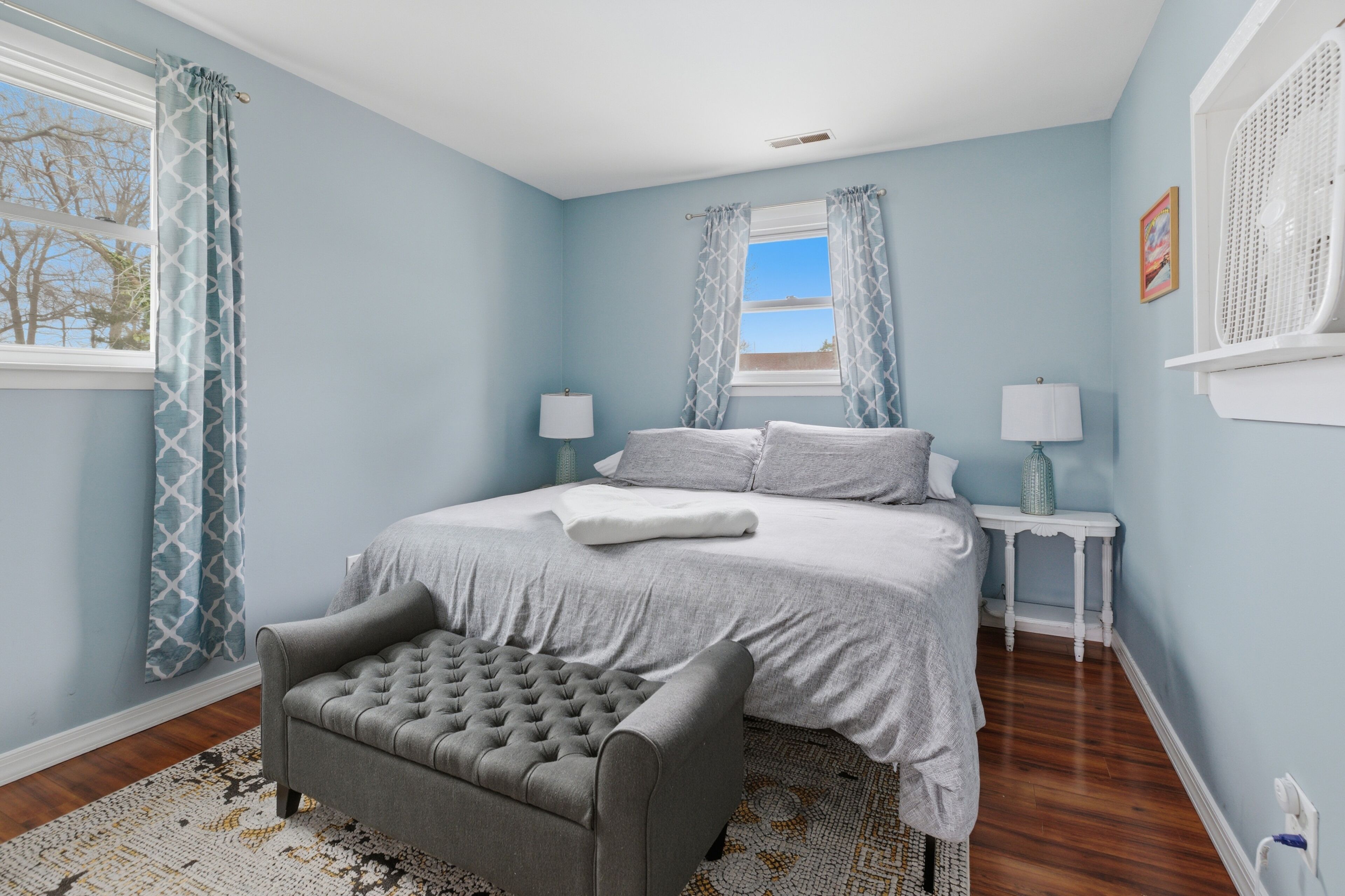 A bedroom with a bed, two bedside tables, a chair, and a window with curtains.