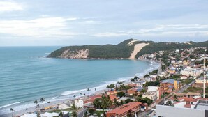 A coastal town with a beach, buildings, and a hill with a path. - Apart em Ponta Negra por Carpediem (Natal)