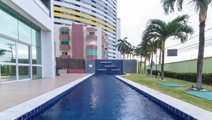 A swimming pool with a modern building in the background. - Apart em Ponta Negra por Carpediem (Natal)