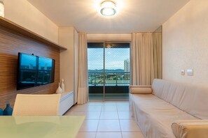 Relax in this stylish living room with a large flat-screen TV, comfortable sofa, and armchair, plus a balcony with a city view.
