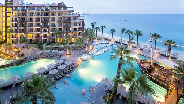 Un resort con varias piscinas, palmeras y un edificio grande con balcones con vistas al mar.