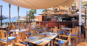Un restaurant en plein air avec des tables et des chaises en bois, un coin bar et une vue sur la mer.
