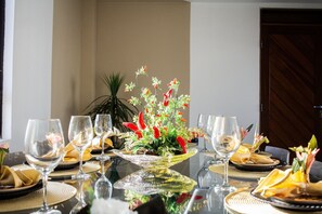 Ein Esstisch ist gedeckt mit Gläsern, Tellern und Servietten, mit einem Blumenarrangement in der Mitte.