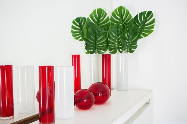 A white shelf with red and white glass vases and red spherical objects.