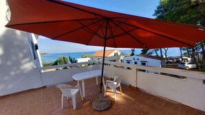 A balcony with a red umbrella, white chairs, and a round table.