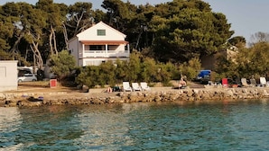 A coastal property with a white building, a stone wall, and a row of beach chairs.