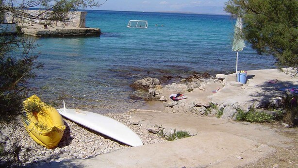 A beach with clear water, a surfboard, and a kayak.