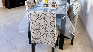 Un comedor con una mesa preparada para seis personas, rodeada de sillas con diseño. Un mueble de entretenimiento negro está contra la pared de ladrillo, y se ve una puerta al fondo.