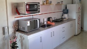 Una cocina con armarios blancos, microondas, hervidor y refrigerador.