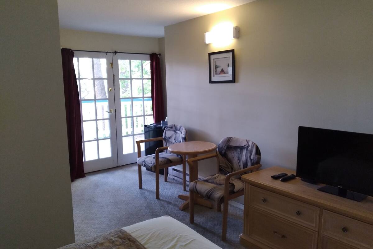 A hotel room with a bed, a desk with a chair, a television, and a window with curtains.