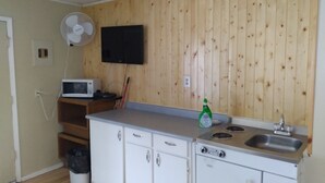 Una cocina compacta con paneles de madera, un microondas, un lavamanos y un ventilador.