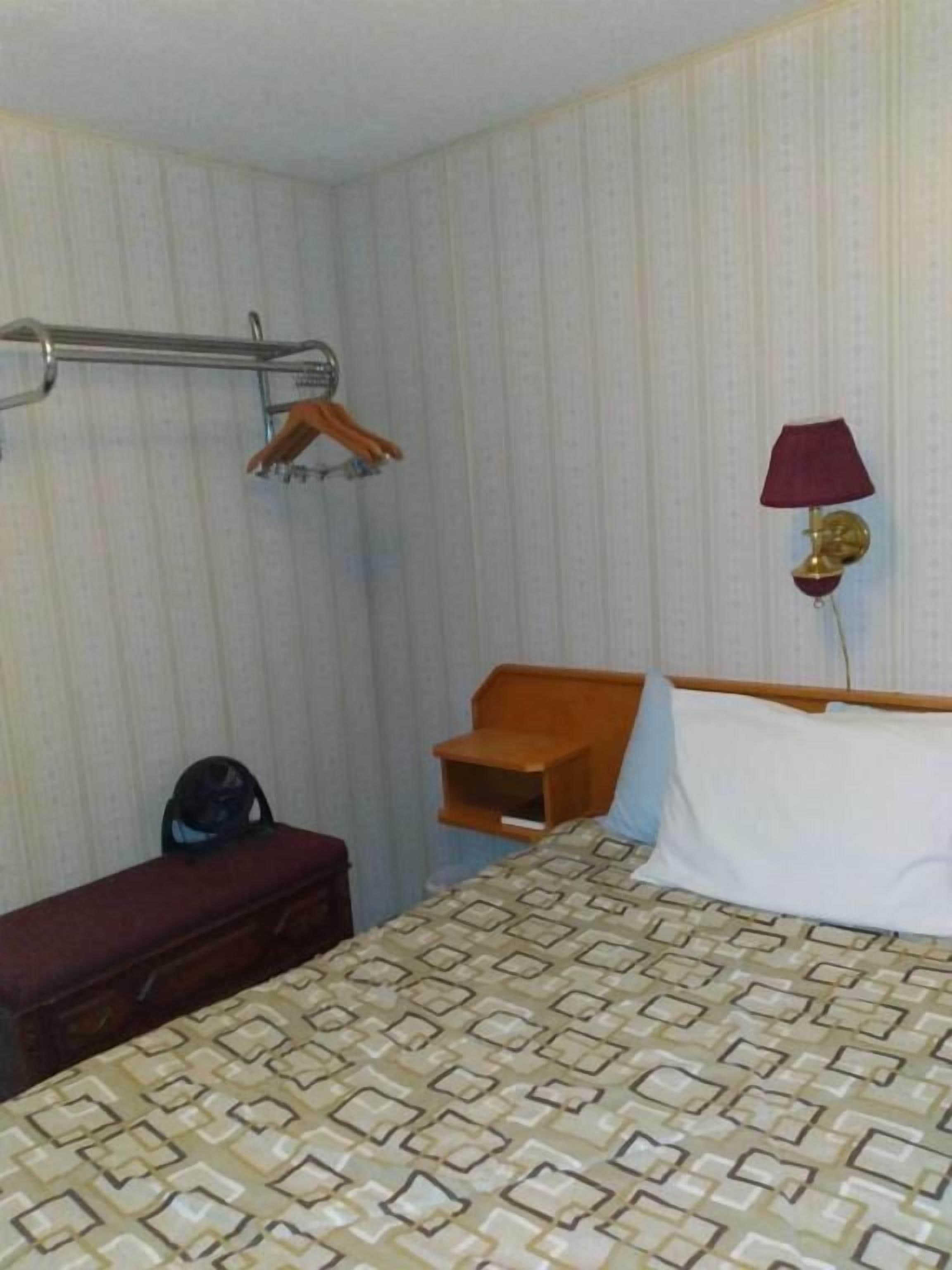 Une chambre d’hôtel avec un lit, un banc en bois, une petite table, un porte-manteau mural et une lampe fixée au mur.