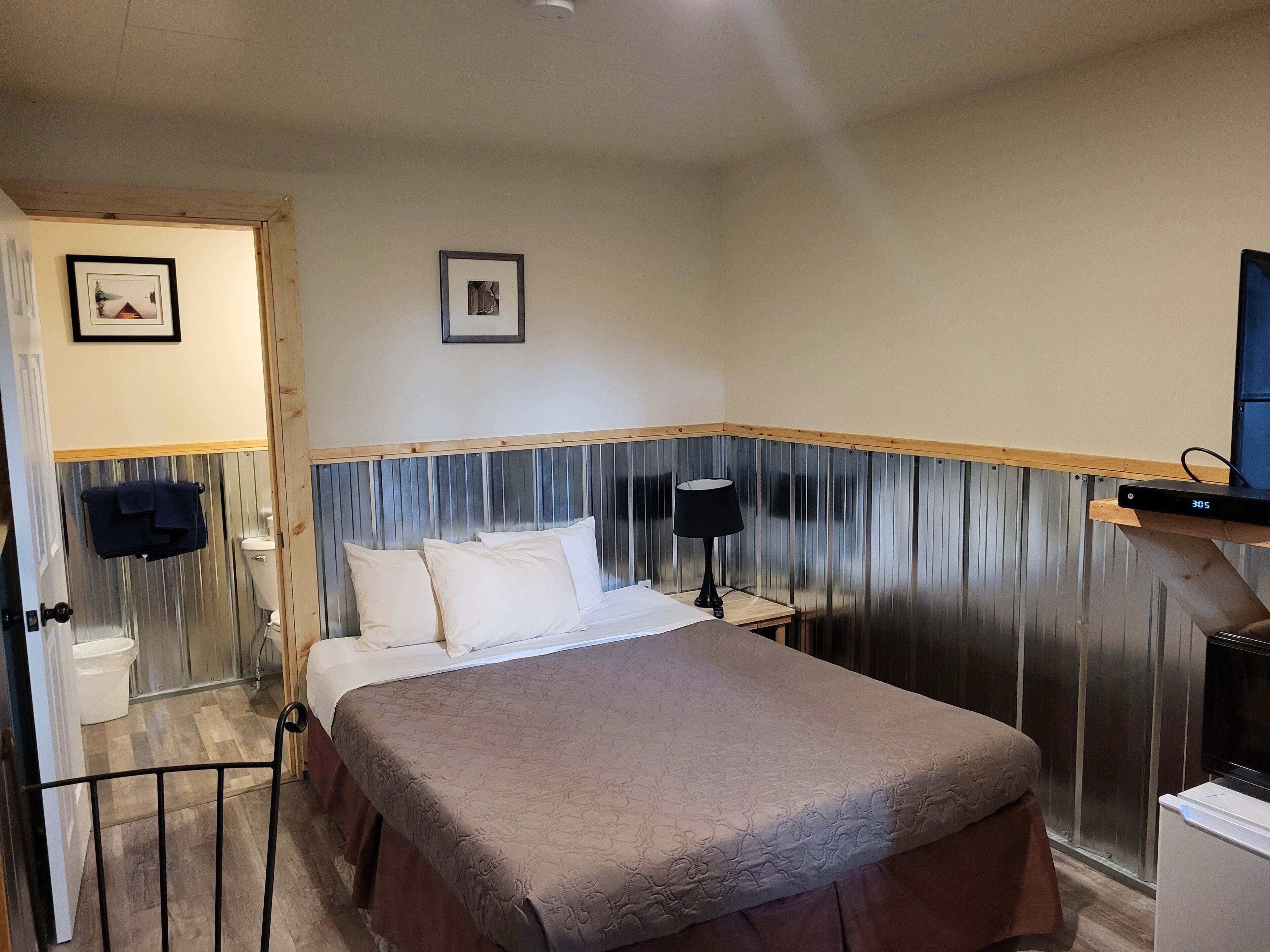 A bedroom with a bed, a bedside table with a lamp, a TV, and a small cabinet.