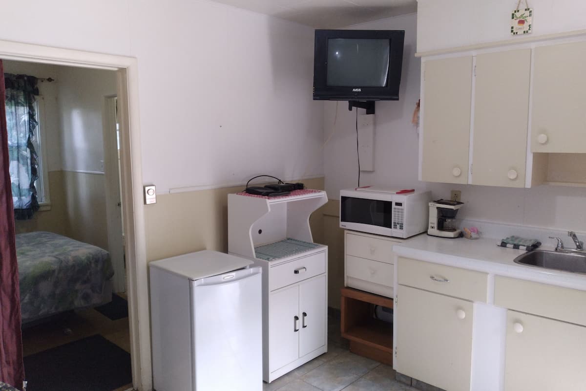 A compact kitchen with a microwave, a small refrigerator, a television, and basic cabinetry.