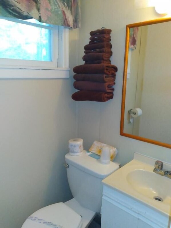 A small bathroom with a toilet, sink, and a stack of towels hanging on the wall.