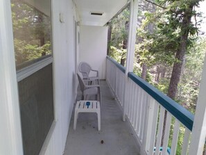 A covered porch with two white plastic chairs and a small table, surrounded by a white railing with a green top.
