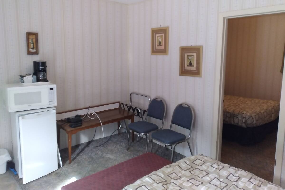 A small hotel room with a bed, a desk with a microwave, two chairs, and a refrigerator.