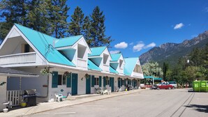 Una hilera de edificios blancos con techos azules, con mesas al aire libre y montañas al fondo.