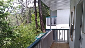 Terraza de madera con baranda blanca, con vista a un área boscosa.