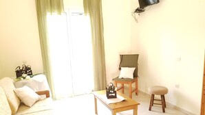 A well-lit living room with a sofa, a wooden coffee table, a chair, and a small stool. - Corfu Escape Three (Corfu)